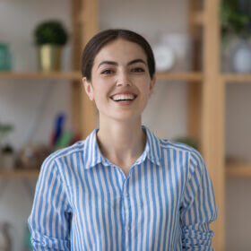 Economics: Smiling woman in striped shirt in front of bookshelf. Professional business portrait.